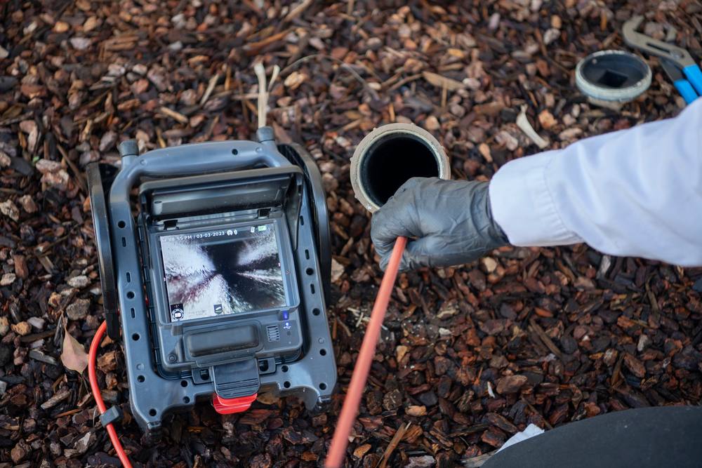 Technician feeding a sewer inspection camera into a cleanout, monitor showing inside the pipe